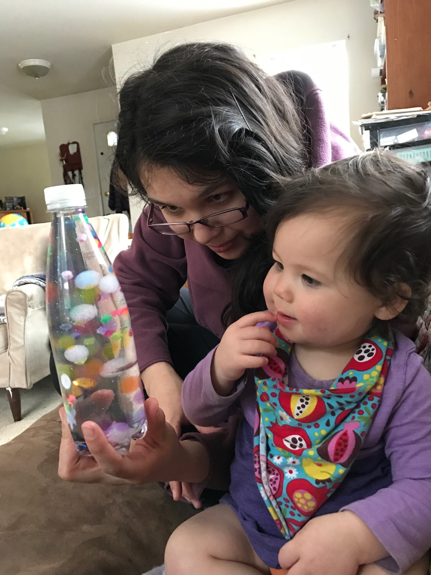 A child looks at a sensory bottle held by an adult